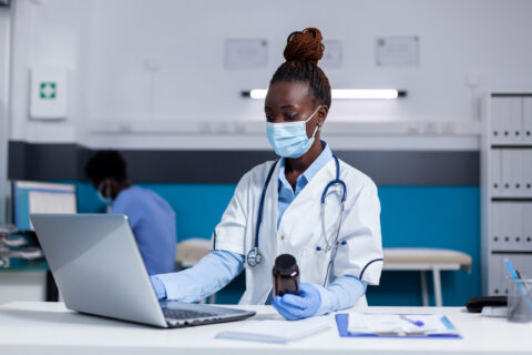 African american woman with doctor job holding bottle of medicine