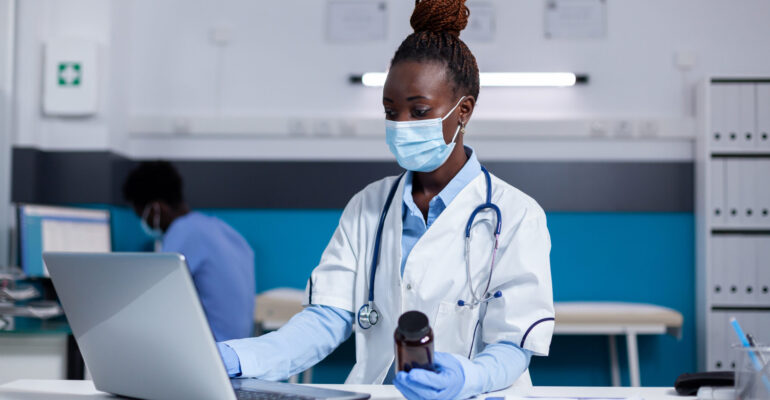 African american woman with doctor job holding bottle of medicine