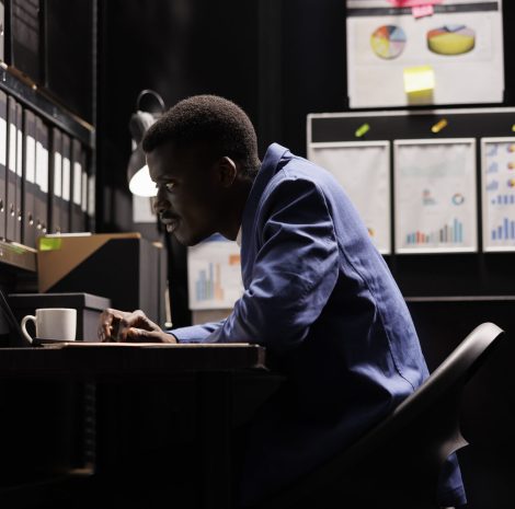 African american secretary looking at bookkeeping files, analyzing administrative documents late at night in storage room. Businessman discovering bureaucracy report, checking accountancy paperwork