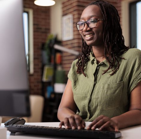 Smiling african american programmer relaxing looking at funny content on computer screen while typing on keyboard. Freelancer laughing with friends while chatting using pc in home living room.