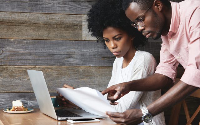 Two corporate workers dressed casually discussing new project. African man in spectacles holding papers explaining details of report to his African female colleague who is listening to him attentively